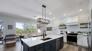 A modern kitchen with a large island, stainless steel appliances, and a view to the outdoors. - Mango Bay – Luxury Island Home w/ Heated Pool, Spa & Walk To Beach (Holmes Beach)