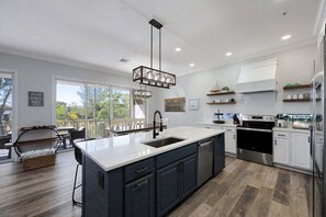 A modern kitchen with a large island, stainless steel appliances, and a view to the outdoors. - Mango Bay – Luxury Island Home w/ Heated Pool, Spa & Walk To Beach (Holmes Beach)