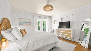 A bedroom with a large bed, a television, a dresser, and a painting on the wall. - The Cottage on Pine - Charming Pine Ave Cottage w/ Heated Pool in Heart of AMI (Anna Maria)