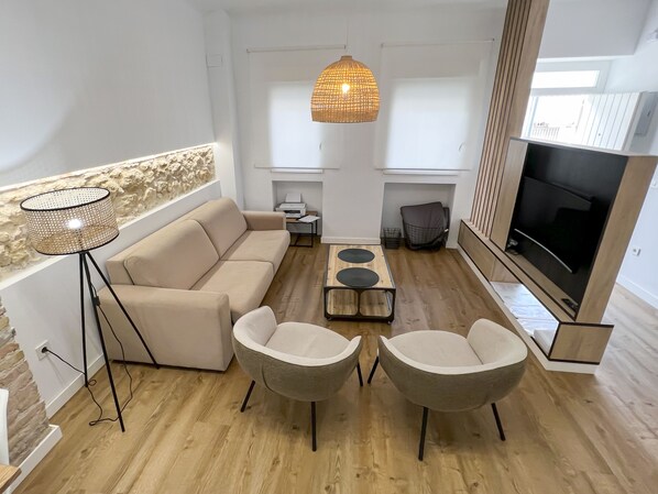 A modern living room with a sofa, two armchairs, a coffee table, a floor lamp, a TV, and a fireplace. - Apartment (Córdoba)