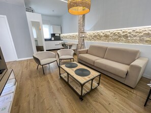 Uma sala de estar moderna com um sofá, duas poltronas, uma mesa de centro e um espaço de refeições ao fundo.