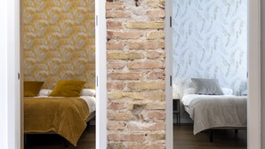 Une vue partagée de deux chambres à coucher, chacune ayant un motif de papier peint différent, avec un mur en briques et un plancher en bois.