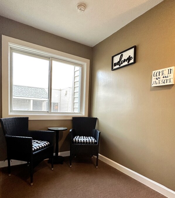 A room with two wicker chairs and a small table, a large window, and two motivational wall signs.