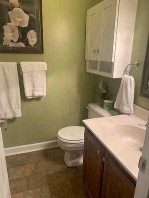 Une petite salle de bain avec des toilettes, un lavabo et un meuble de rangement. Deux serviettes blanches sont accrochées au mur.