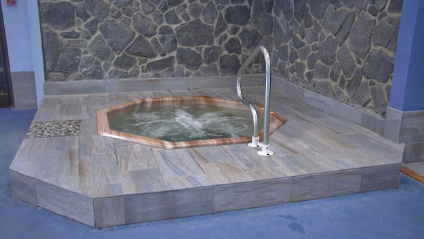 Een stenen muur, een hottub met houten rand en een metalen trap.