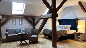 A loft bedroom with exposed wooden beams, a bed with a dark headboard, a sofa, a chair, and a small table. - Schloss Schlemmin (Schlemmin)