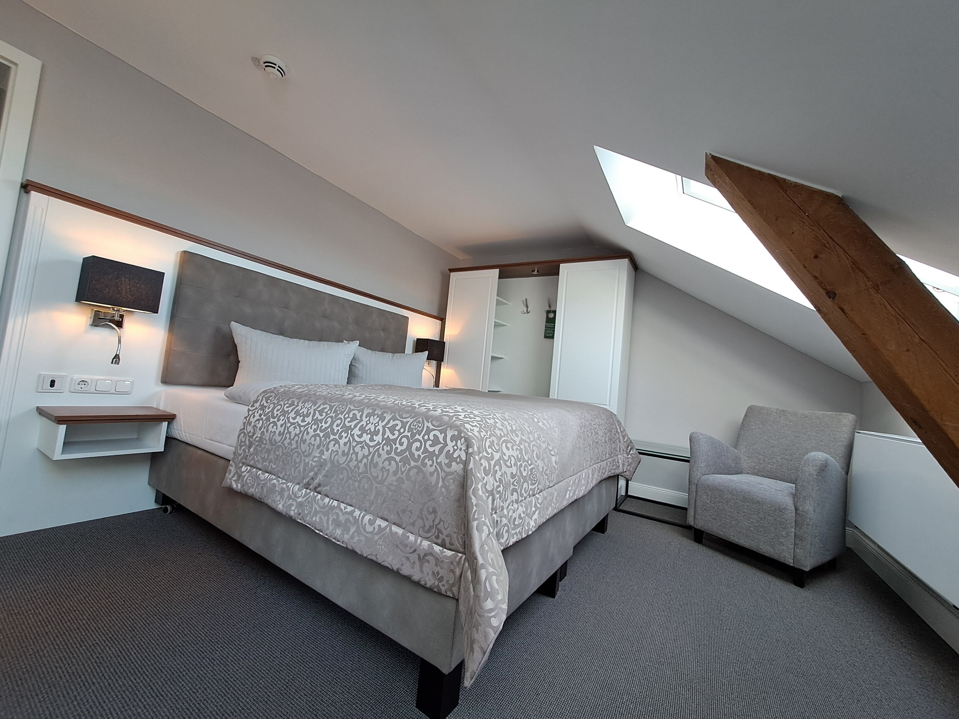 Een moderne slaapkamer met een groot bed, een nachtkastje, een stoel en een dakraam.