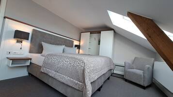 A modern bedroom with a large bed, a bedside table, a chair, and a skylight.