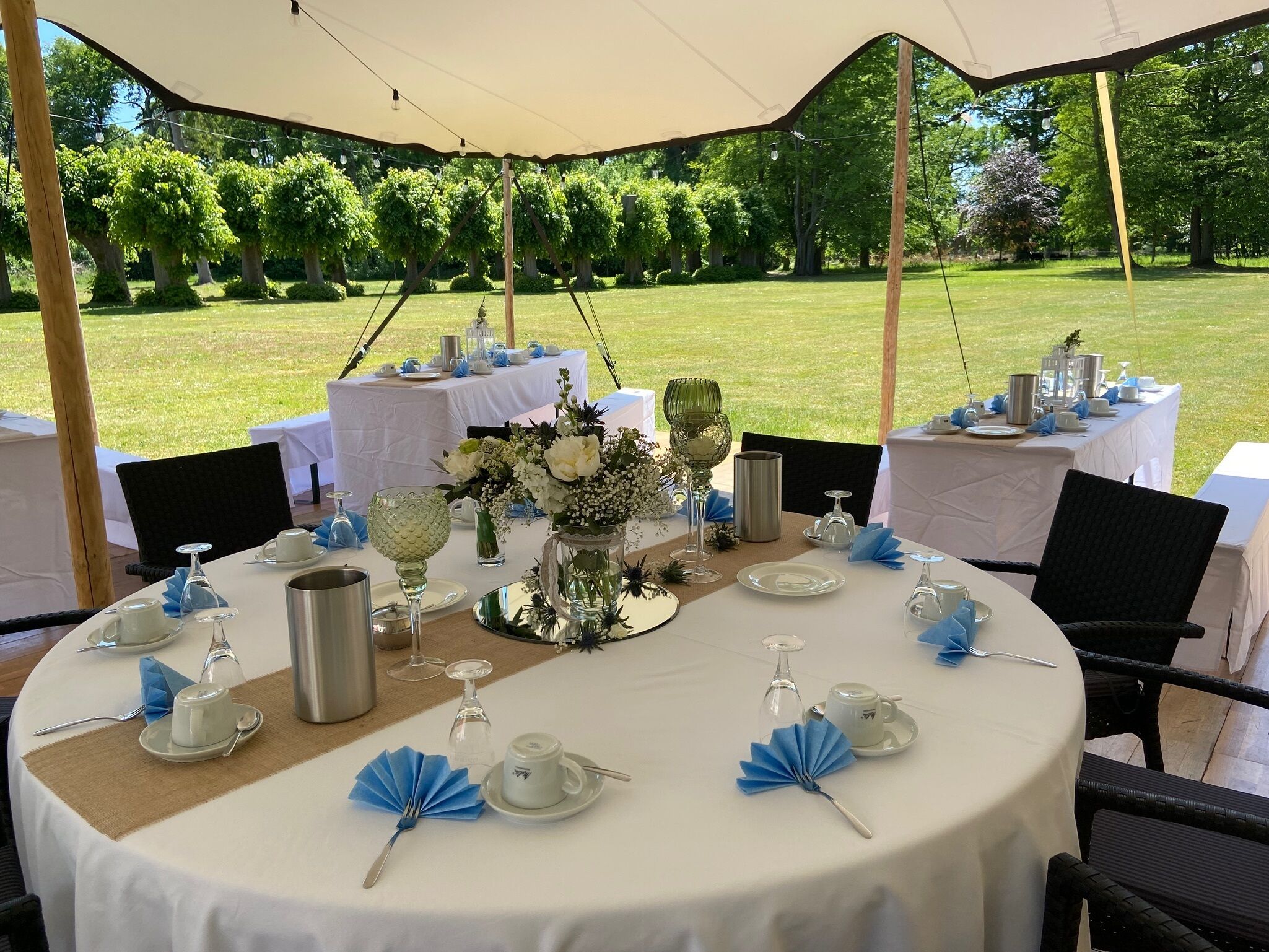 Een buitenterras met ronde tafels gedekt voor een maaltijd, omringd door een tent.