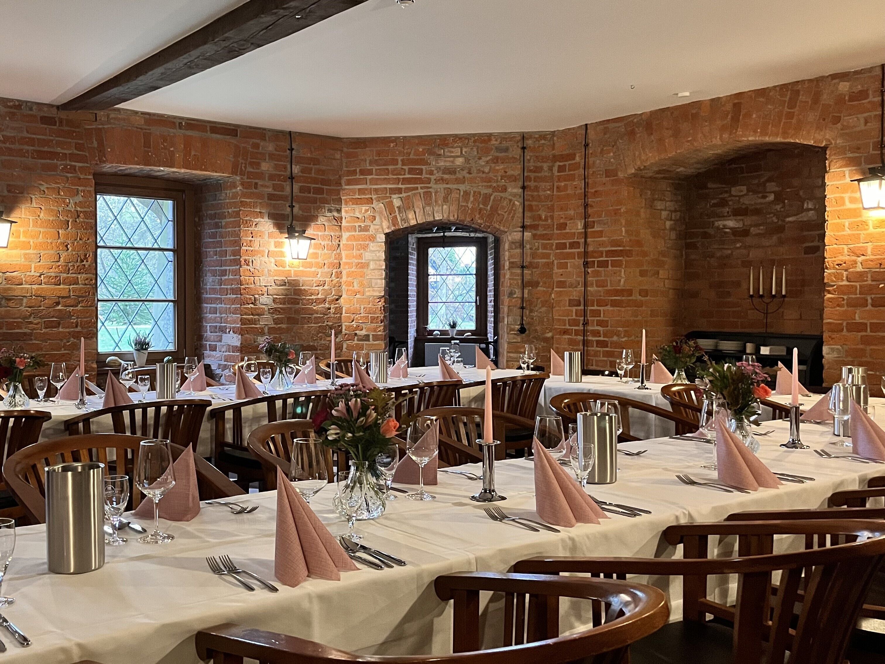 A restaurant with brick walls, large windows, and tables set with white tablecloths, silverware, and glassware.