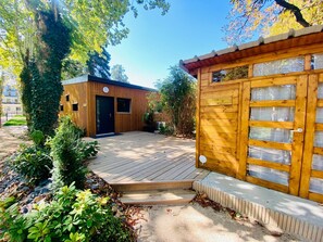 A wooden building with a garage door, surrounded by a wooden deck and greenery. - Eco-cottage with private spa  (Saint-Affrique)