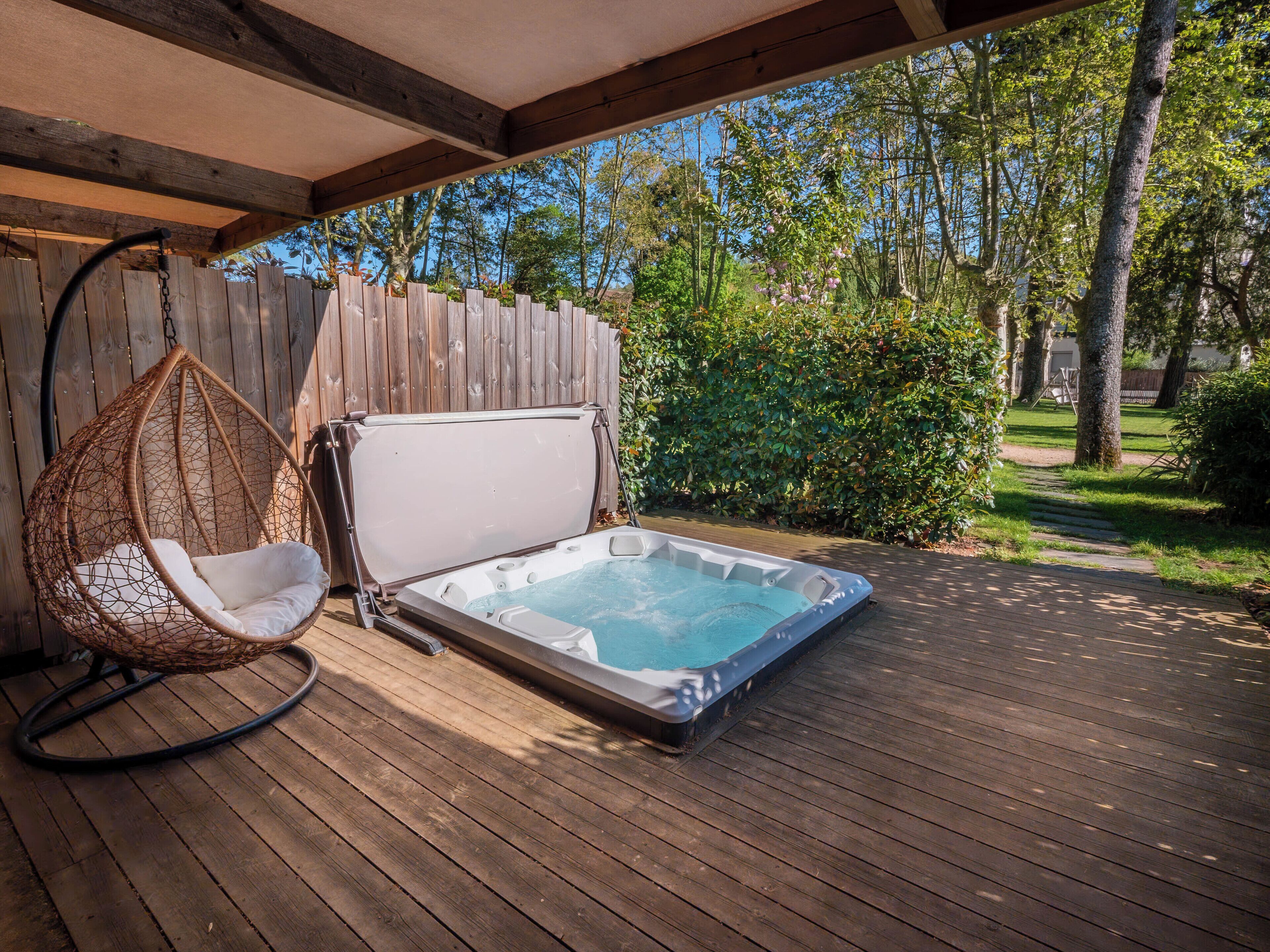 Een hottub op een houten terras, met een hangstoel en een houten omheining op de achtergrond.