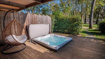 Een hottub op een houten terras, met een hangstoel en een houten omheining op de achtergrond.