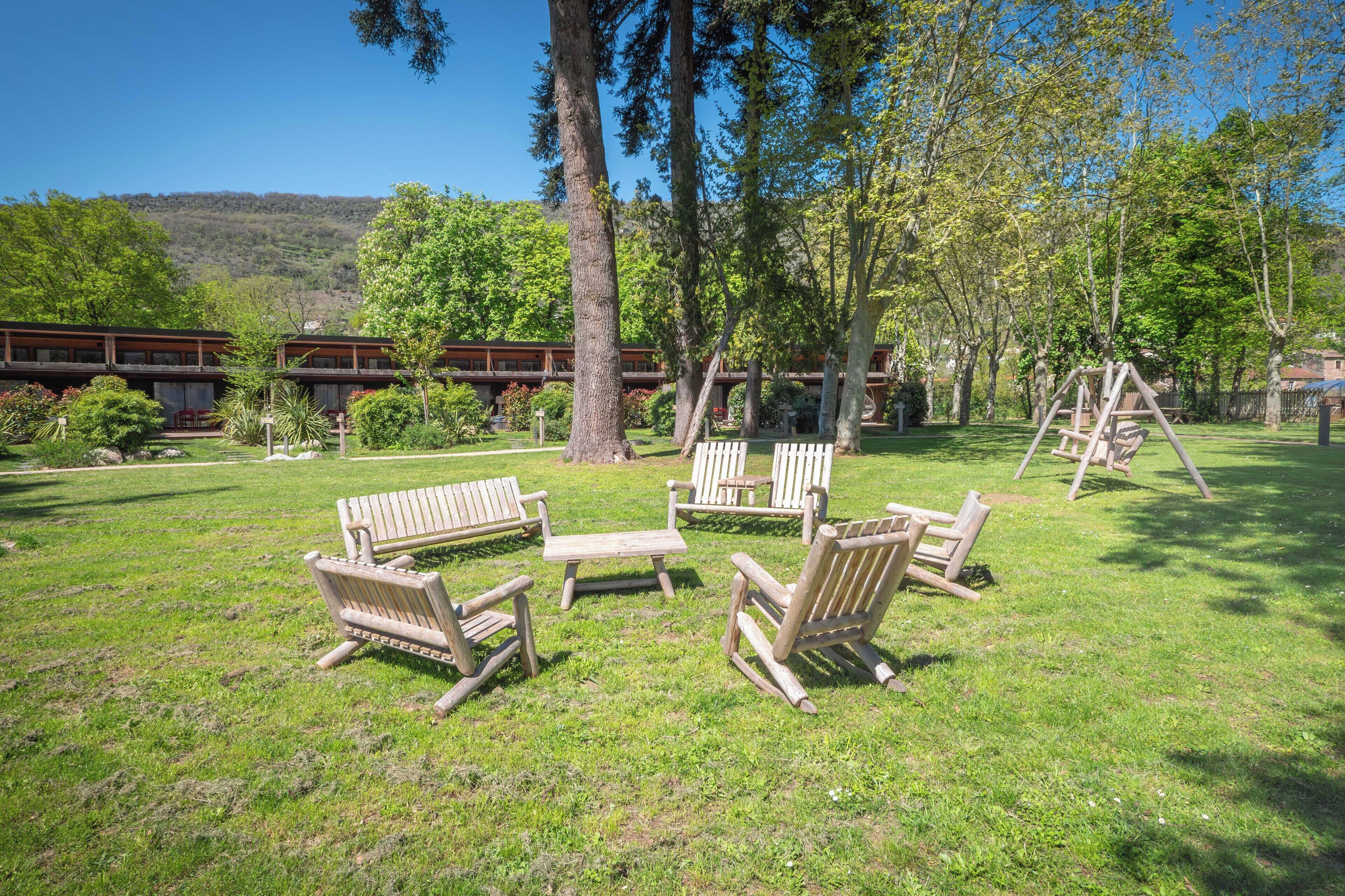 A grassy outdoor area with wooden benches and a swing set.