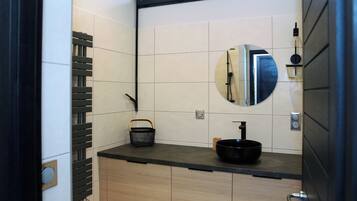 Un baño moderno con un lavabo negro, un espejo redondo y un mueble de madera.
