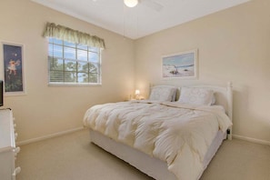 Une chambre à coucher avec un lit, une fenêtre avec des stores, un ventilateur de plafond et un tableau accroché au mur.
