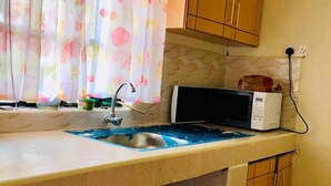 A small kitchen with a microwave, a sink, and wooden cabinets. - Stay.Plus Arujo Apartment Homa Bay (Homa Bay)