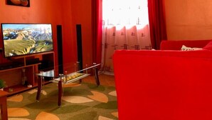 A living room with a red sofa, a television on a wooden stand, and a glass coffee table. - Stay.Plus Arujo Apartment Homa Bay (Homa Bay)