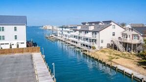 A waterfront property with a dock, a row of white buildings, and a clear view of the water. - Large Waterfront Townhome with Boat Dock and Pool (Ocean City)