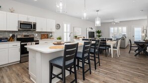 A modern kitchen with white cabinets, a central island, and a dining area with chairs. - Large Waterfront Townhome with Boat Dock and Pool (Ocean City)