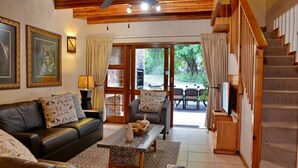 A cozy living room with a leather sofa, a coffee table, and a staircase leading to an outdoor area. - Cambalala Unit 4  - Luxury Self Catering Vacation Rental In Kruger Park Lodge (Hazyview)