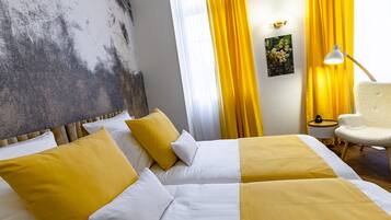Ein Hotelzimmer mit zwei Betten, gelb-weißer Bettwäsche, einer weißen Lampe, einem Sessel und einem Bild an der Wand.