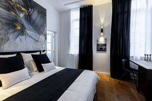 Una habitación de hotel moderna con una cama grande, un escritorio y un cuadro abstracto blanco y negro en la pared.