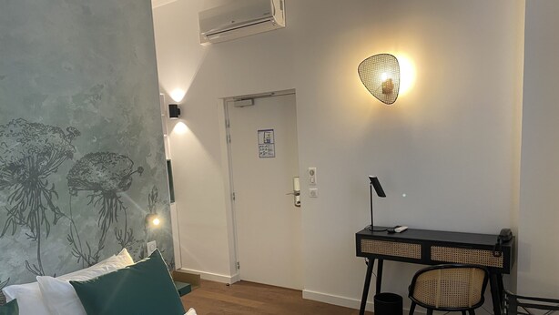 A bedroom with a bed, a desk, and a chair. There is a wall-mounted light fixture and an air conditioning unit. - Hotel du Palais (Dijon)