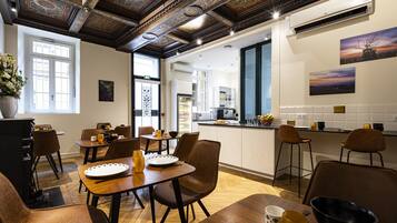 Un comedor con mesas y sillas de madera, una cocina al fondo y obras de arte en las paredes.