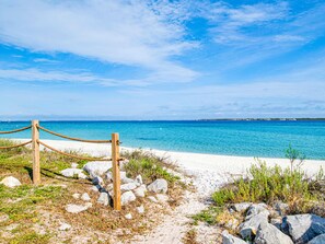 A beach with a wooden fence and rope barrier, leading to a sandy shore with clear blue water and a distant shoreline. - Palm Beach Club #247 | Beach Access, Gulf Views! (Pensacola Beach)