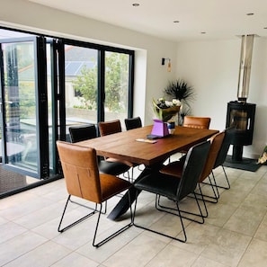 A dining area with a wooden table and chairs, a vase of flowers, and a wood-burning stove. - Captivating 5-bed House in Porthleven (Helston)