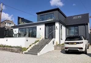 A modern two-story house with a white exterior, a grey roof, and a white car parked in front. - Captivating 5-bed House in Porthleven (Helston)
