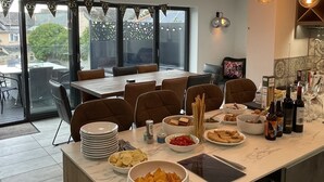 A modern dining area with a large table, chairs, and a variety of food and drink items. - Captivating 5-bed House in Porthleven (Helston)