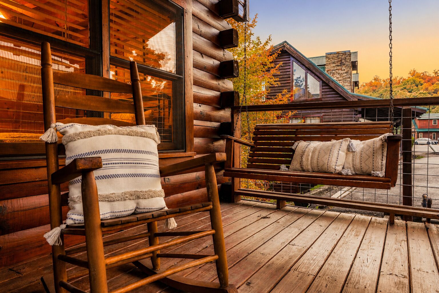 Una mecedora de madera con cojín y una silla colgante con cojines en una terraza de madera.