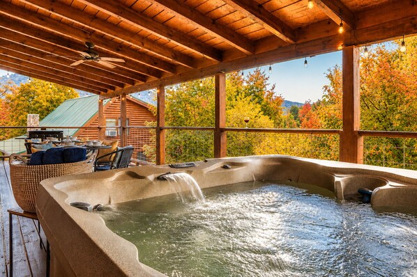 A hot tub with a waterfall feature, surrounded by wicker furniture and a wooden deck.