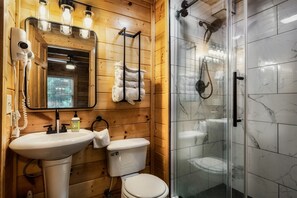 A wooden cabin bathroom with a sink, toilet, and glass-enclosed shower.