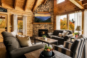 A cozy cabin interior with a stone fireplace, comfortable seating, and a large window offering a scenic view.