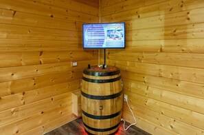 A wooden cabin interior with a wooden barrel, a mounted television, and a power outlet.