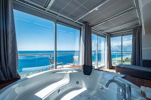 Una habitación moderna con un ventanal grande, bañera de hidromasaje y vista al océano.