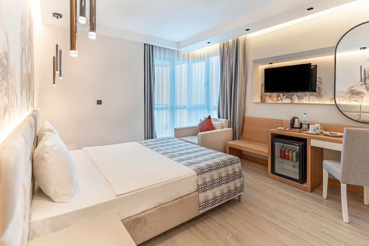 Une chambre d’hôtel moderne équipée d’un lit, d’un bureau avec un mini-réfrigérateur, d’une télévision et d’un coin salon comprenant un canapé et un fauteuil.