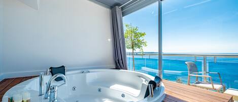 Une salle de bain moderne avec une grande baignoire, une terrasse en bois et une vue sur l’océan.