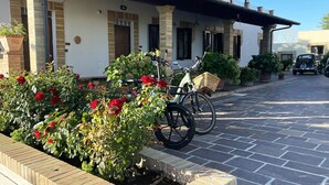 A street view with a white building with black shutters, a bicycle parked in front, and a row of red flowers. - 2-bed Apartment in Abruzzo, Italy 15 Minute to sea (Paglieta)