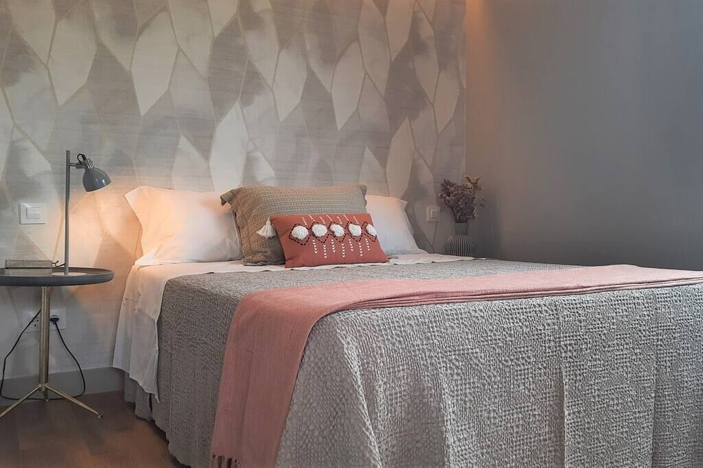 A neatly made bed with a textured blanket, a bedside lamp, and a wall with a geometric pattern.
