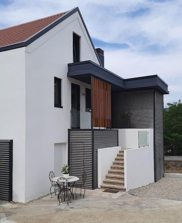 A modern two-story house with a white exterior, a red-tiled roof, and a staircase leading to the upper floor.