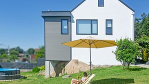Una casa moderna con piscina, un patio con mesa y sillas, y una sombrilla grande.