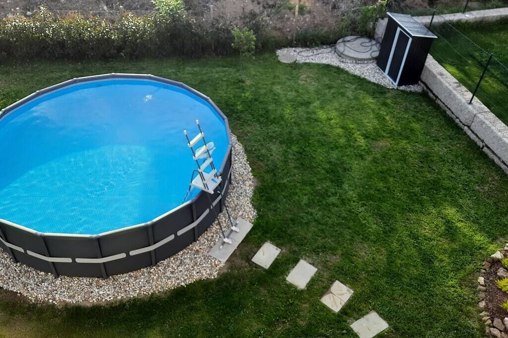 An octagonal swimming pool with a ladder, surrounded by a pebble border and a well-maintained lawn.