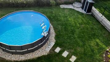 An octagonal swimming pool with a ladder, surrounded by a pebble border and a well-maintained lawn.