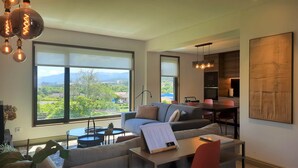 Una sala de estar moderna con ventanas amplias, un sofá, una mesa de comedor y una zona de cocina.