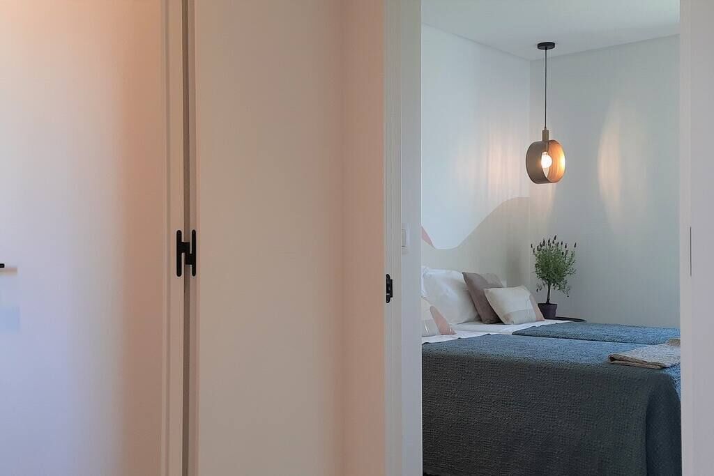 Een slaapkamer met een bed, kussens, een kleine plant in een pot en een hangende lamp.