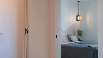 Een slaapkamer met een bed, kussens, een kleine plant in een pot en een hangende lamp.